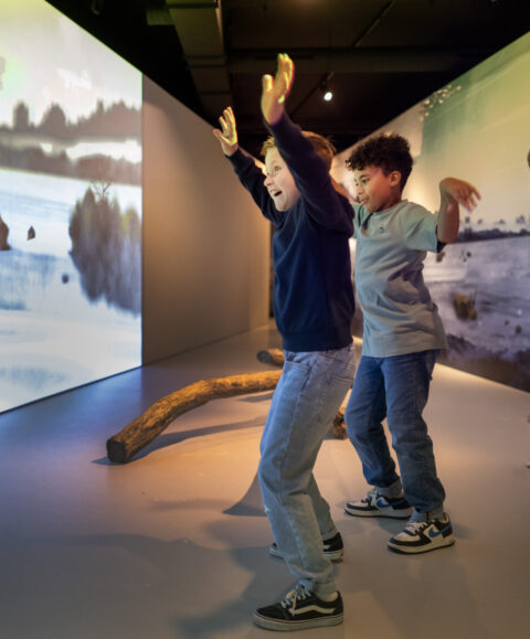 Kinderen in de 'Zaal van de Mens' proberen de mammoet bang te maken door wild met hun armen te zwaaien.